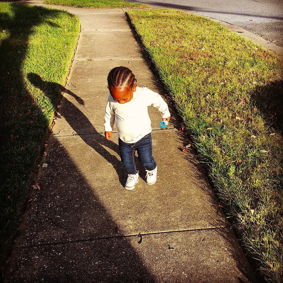 Zaine is registered to the contest to win money with this photo: asphalt, baby, child, concrete, denim, garden, grass, green, groundcover, human, jeans, lawn, people_in_nature, person, play, shadow, sidewalk, toddler, walking, walking_shoe