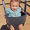 toddler, child, playground, swing, smiling, happy, outdoor, portrait, playground_equipment, wood_chips, sunlight, shadow, chains, seated, blue_shirt, brown_hair, face, hands, legs, joy