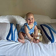 Leïa participe au concours pour gagner de l'argent avec cette photo : baby, child, bed, pillow, striped_pillow, blue_outfit, hat, smiling, indoor, headboard, white_bed_sheet, barefoot, infant, sitting, cute, happy, person, portrait, plush, furniture