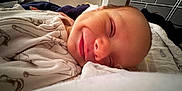 Riley-James is registered to the contest to win money with this photo: baby, newborn, smiling, sleeping, close_up, blanket, bedroom, cozy, infant, face, soft, cute, resting, child, indoors, warm_light, peaceful, clothing, portrait, happy