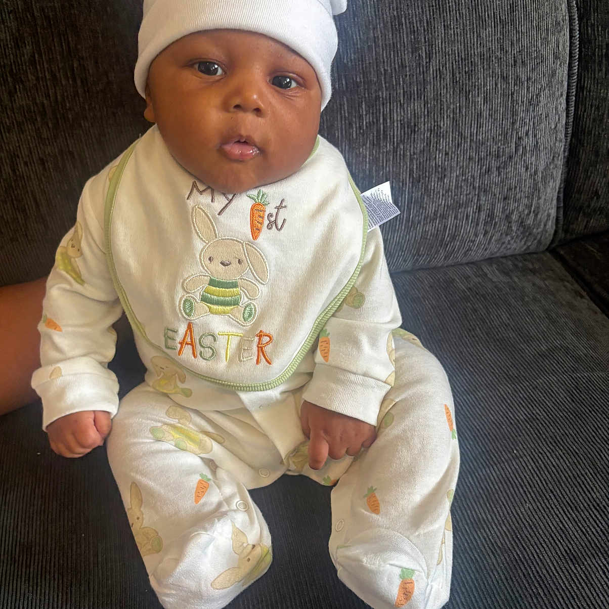 Lávon joined the competition — help win amazing prizes! baby, bonnet, cap, clothing, couch, cushion, face, formalwear, furniture, glove, hat, head, newborn, pants, person, photography, portrait, sitting, standing, suit