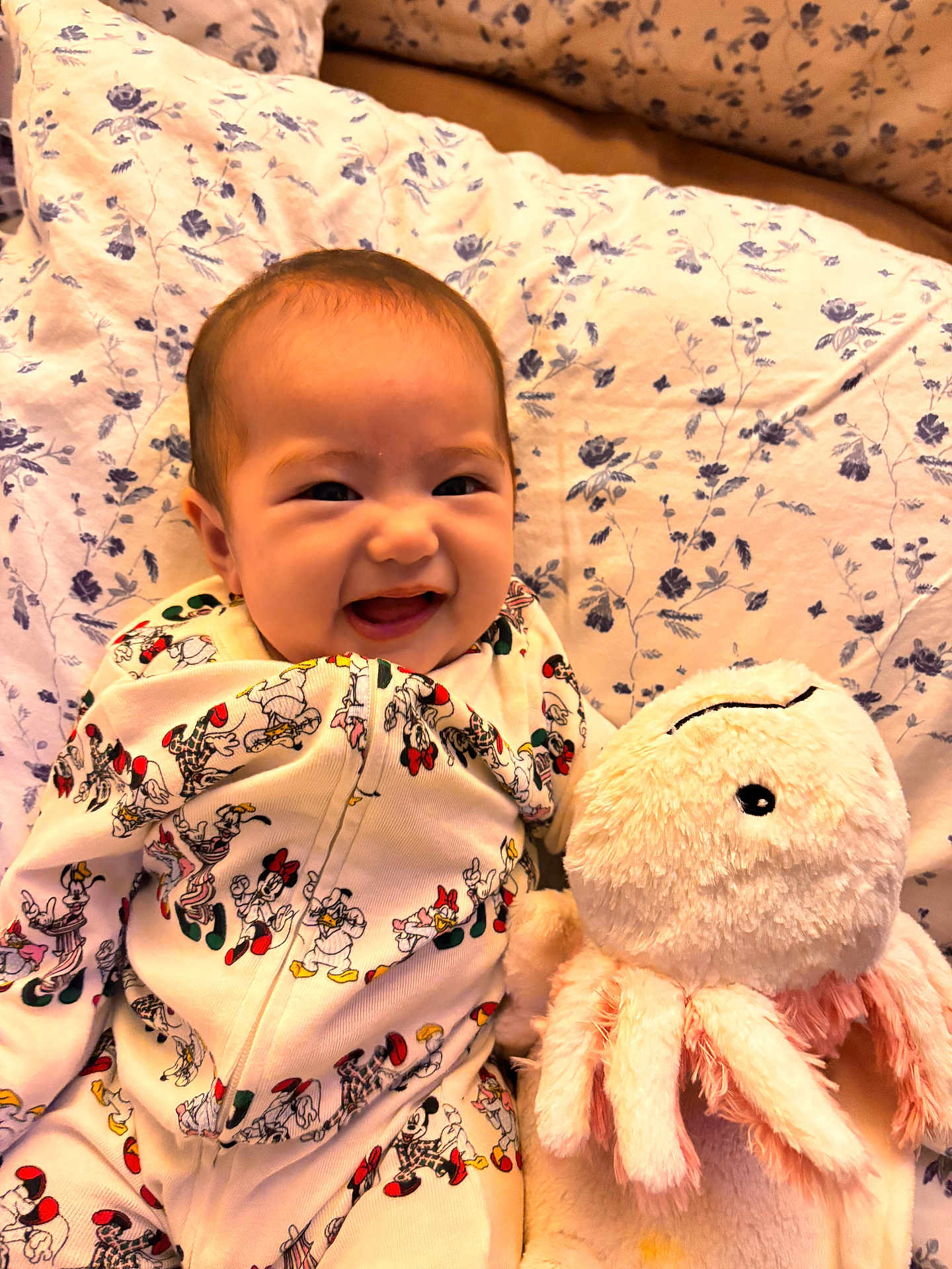 Ellie Victoria is registered to the contest to win money with this photo: baby, smiling, onesie, mickey_mouse, minnie_mouse, plush_toy, octopus, bed, blanket, floral_pattern, cute, infant, child, soft_toy, happy, indoors, portrait, cuddly, cozy, sleepwear