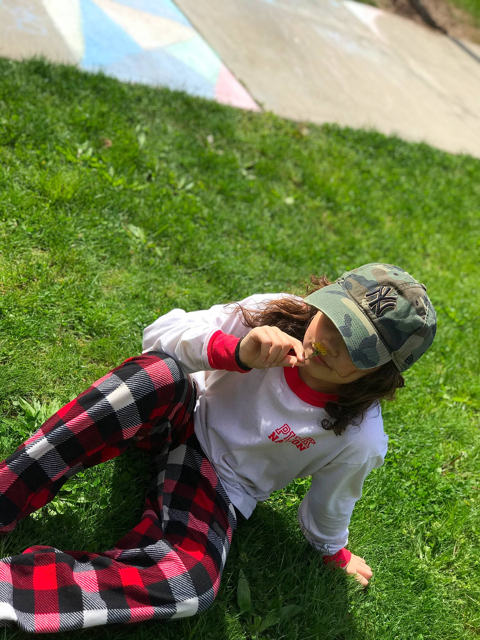 Kelli is registered to the contest to win money with this photo: baseball_cap, clothing, competition_event, fun, grass, grassland, hat, lawn, leisure, pattern, people_in_nature, person, plaid, plant, player, recreation, sitting, sports, t_shirt, tartan
