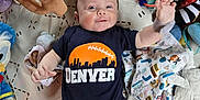 Isiah is registered to the contest to win money with this photo: baby, infant, onesie, denver, football, plush_toy, blanket, patterned_blanket, colorful, smiling, reaching, lying_down, baby_accessories, cute, child, indoors, soft_toys, blue_clothing, orange_logo, happy
