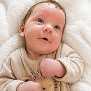 ëlio participe au concours pour gagner de l'argent avec cette photo : baby, infant, child, blue_eyes, smile, cozy, blanket, beige_clothing, cute, portrait, soft_texture, fuzzy, lying_down, happy, young_child, face, skin, small_hands, indoors, warm