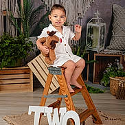 Liam joined the competition — help win amazing prizes! toddler, child, toy, plush, reindeer, ladder, wooden, step_ladder, white_clothing, smiling, indoor, plants, greenery, macrame, boho_decor, crate, candle_lantern, rug, birthday, letters