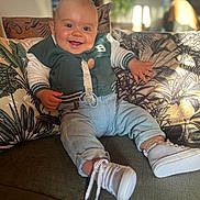 Rafaël a rejoint le concours — aidez-le/la à gagner de superbes lots ! baby, smiling, indoor, couch, pillow, green_jacket, denim_pants, white_shoes, pacifier_clip, happy, child, cute, face, feet, hand, home, sunlight, plant, cozy, portrait