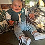 baby, smiling, indoor, couch, pillow, green_jacket, denim_pants, white_shoes, pacifier_clip, happy, child, cute, face, feet, hand, home, sunlight, plant, cozy, portrait