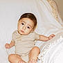 baby, infant, child, onesie, beige_clothing, couch, blanket, white, texture, sitting, curious_expression, indoors, soft_light, portrait, cute, small_hands, small_feet, face, young_child, relaxed