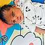 Sri Thanvik is registered to the contest to win money with this photo: baby, newborn, infant, child, bed, blanket, cartoon, pattern, dog_print, clothing, cute, face, lying_down, colorful, soft, young, portrait, skin, hand, eyes