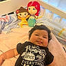 baby, bedroom, black_shirt, blanket, child, cozy, crib, curly_hair, cute, doll, happy, indoor, infant, person, plush_toy, resting, smile, soft_toys, text_on_clothing, toddler