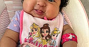 Zoé Jimena joined the competition — help win amazing prizes! baby, bib, cartoon, child, closeup, curly_hair, cushioned_seat, cute, happy, indoors, infant, person, pink, playful, princess, purple, smiling, tongue_out, unicorn, wristband