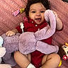 baby, blanket, child, curly_hair, cute, doll, floor, happy, indoors, infant, lying_down, person, pink, playful, red_clothing, smiling, socks, soft_toy, stuffed_animal, toy