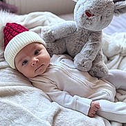 Delilah is registered to the contest to win money with this photo: baby, infant, hat, knit_hat, plush_toy, reindeer, blanket, soft_toy, red_nose, white_clothing, sleepwear, bedroom, cozy, cute, child, portrait, indoors, holiday, winter, resting