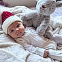 baby, infant, hat, knit_hat, plush_toy, reindeer, blanket, soft_toy, red_nose, white_clothing, sleepwear, bedroom, cozy, cute, child, portrait, indoors, holiday, winter, resting