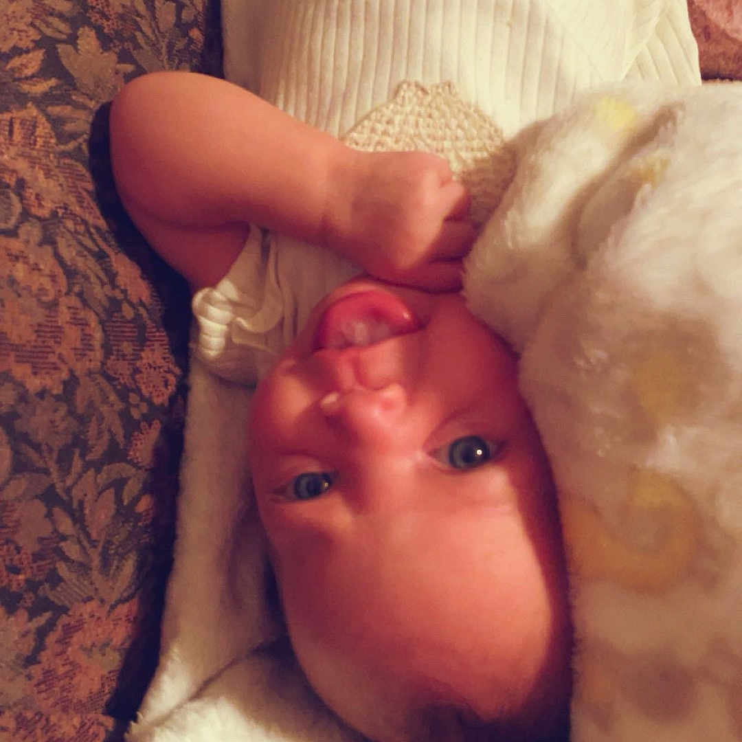 Xayla is registered to the contest to win money with this photo: baby, infant, blanket, lying_down, face, expression, cute, soft_texture, patterned_fabric, child, indoors, warm, cozy, skin, head, eyes, hand, comfort, resting, playful