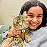 Sonic is registered to the contest to win money with this photo: person, cat, tabby_cat, indoor, smiling, dreadlocks, couch, cozy, collar, tag, closeup, happy, pet, animal, feline, texture, wall, hand, casual_clothing, relaxed