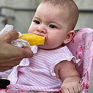 Madison is registered to the contest to win money with this photo: baby, child, cute, expression, feeding, floral_pattern, food, fruit, hand, high_chair, infant, outdoor, person, pineapple, pink, portrait, sitting, skin, striped_clothing, summer