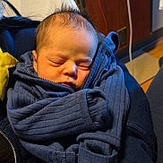 Edward is registered to the contest to win money with this photo: baby, blanket, blue_clothing, chair, close_up, cozy, face, hospital, indoors, infant, knitwear, medical_room, newborn, peaceful, photography, portrait, resting, scarf, sleeping, swaddled