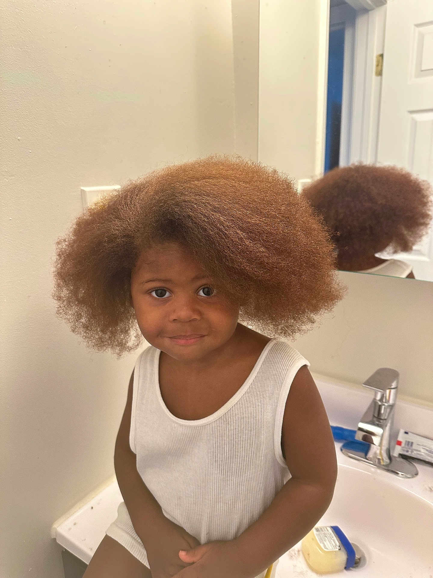 Jamos is registered to the contest to win money with this photo: child, afro_hair, bathroom, sink, mirror, white_shirt, smile, cute, person, reflection, counter, indoor, young_child, hair, face, casual, portrait, skin, faucet, container