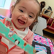 Shaniyah Avangelina joined the competition — help win amazing prizes! toddler, child, smiling, pigtails, pink_dress, bib, indoor, quilt, colorful, furniture, window, happy, face, person, hand, toy, home, cute, baby, playful