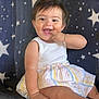 baby, child, smiling, happy, sitting, tank_top, striped_skirt, barefoot, bracelet, star_pattern, couch, indoor, cute, fingers_in_mouth, young_child, portrait, infant, playful, joyful, closeup