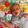 Dillon joined the competition — help win amazing prizes! baby, child, infant, smiling, happy, face, eyes, lying_down, play_gym, colorful, toys, balls, harness, safety_strap, striped_clothing, bed, blanket, indoor, portrait, playtime