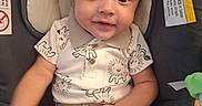 Dillon is registered to the contest to win money with this photo: baby, child, infant, smiling, car_seat, safety_harness, seated, portrait, indoors, clothing, lion_pattern, shirt, pants, brown_hair, face, eyes, happy, vehicle, travel, photography
