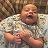 baby, infant, child, smiling, happy, portrait, close_up, sitting, reclining, couch, cushion, pillow, plaid, indoor, home, gray_shirt, clothing, hands, face, photography