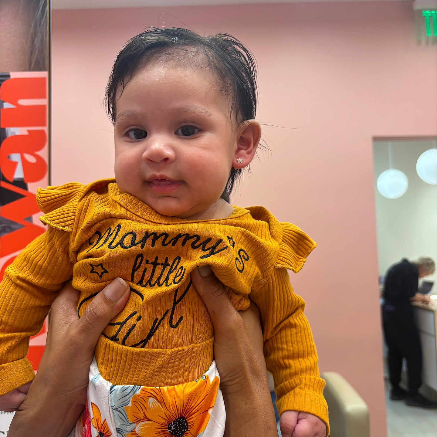 Maddison joined the competition — help win amazing prizes! adult_hands, baby, child, clothing, curly_hair, earrings, expression, face, floral_pants, furniture, hands, holding, indoor, lighting, people, person, room, sitting, wall, yellow_top