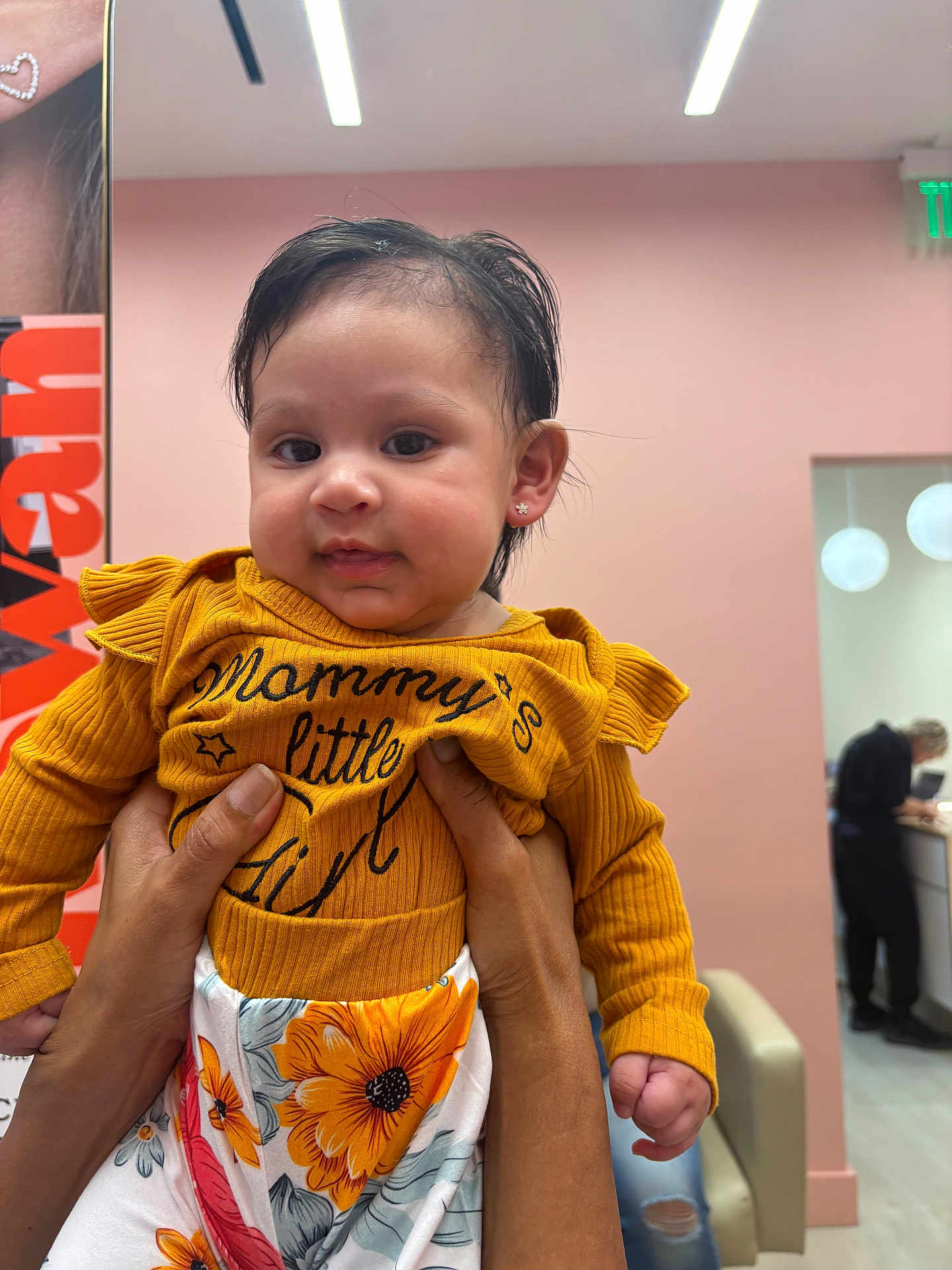 Maddison joined the competition — help win amazing prizes! baby, child, person, indoor, clothing, yellow_top, floral_pants, hands, face, earrings, curly_hair, expression, room, wall, lighting, adult_hands, holding, sitting, furniture, people