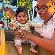 Maddison joined the competition — help win amazing prizes! baby, adult, glasses, slide, playground, outdoor, child, holding, smiling, daylight, park, trees, clothing, person, cute, fun, happy, sunlight, nature, family