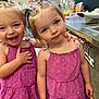 child, toddler, girl, matching_dresses, purple_dress, smiling, laughing, indoor, classroom, playful, hair_tied, cute, happy, friends, person, people, two_children, young, preschool, colorful_background