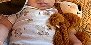 Derecho is registered to the contest to win money with this photo: baby, child, face, aviator_hat, goggles, stuffed_animal, plush_toy, clothing, patterned_background, warning_label, hand, jeans, white_onesie, cute, indoor, portrait, infant, soft_toy, lying_down, expression