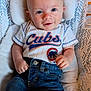 baby, infant, child, cubs_shirt, denim_jeans, smiling, face, head, eyes, hand, cushion, baby_seat, clothing, comfortable, cute, portrait, happy, indoor, casual, young