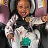 Journei is registered to the contest to win money with this photo: baby, child, car_seat, pink, onesie, strawberry_pattern, smiling, happy, pacifier, curly_hair, safety_harness, infant, cute, indoors, seat, person, closeup, expressive_face, joyful, clothing