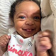Journei is registered to the contest to win money with this photo: baby, smiling, tongue, cute, infant, clothing, white, bedding, happy, face, person, portrait, hand, expression, young, child, cozy, soft, lying_down, closeup