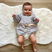 Lise a rejoint le concours — aidez-le/la à gagner de superbes lots ! baby, smiling, infant, floral_shirt, white_rug, wooden_floor, diaper_cover, happy, cute, child, lying_down, indoors, skin, face, hands, legs, barefoot, clothing, portrait, one_person