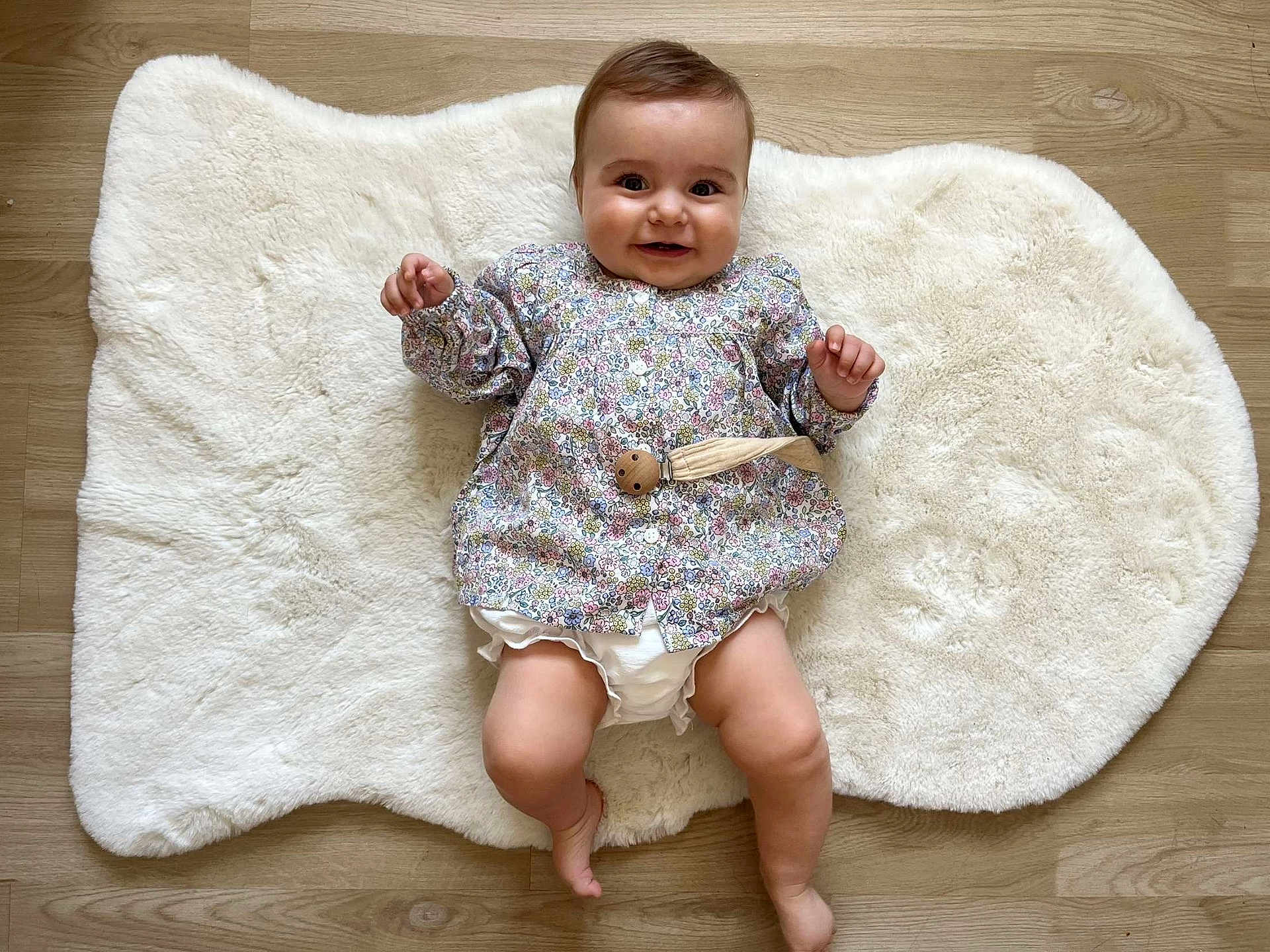 Lise a rejoint le concours — aidez-le/la à gagner de superbes lots ! baby, smiling, infant, floral_shirt, white_rug, wooden_floor, diaper_cover, happy, cute, child, lying_down, indoors, skin, face, hands, legs, barefoot, clothing, portrait, one_person