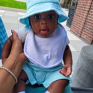 Greyson is registered to the contest to win money with this photo: baby, infant, child, portrait, blue_hat, bucket_hat, bib, blue_clothing, sitting, held, adult_hand, outdoor, courtyard, brick_building, lawn, wide_eyes, open_mouth, baby_socks, baby_shoes, photography