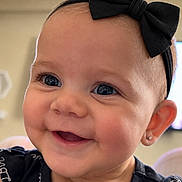 Presley is registered to the contest to win money with this photo: baby, child, infant, portrait, smiling, happy, bow, headband, earring, black_clothing, close_up, face, eyes, indoors, warm_lighting, candid, adorable, sitting, photography, family