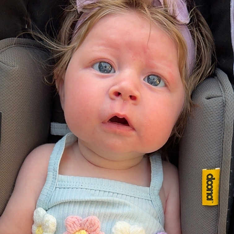 Saylor joined the competition — help win amazing prizes! baby, blue_eyes, car_seat, child, close_up, curly_hair, cute, dress, face, flower, headband, infant, knitted_flower, pastel_colors, pink, portrait, purple, seat_belt, soft_lighting, young_child