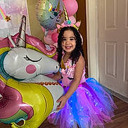 Camila joined the competition — help win amazing prizes! child, girl, toddler, smiling, unicorn, unicorn_costume, birthday, party, balloons, pink, rainbow, dress, tutu, tiara, curly_hair, portrait, indoors, doorway, wood_floor, inflatable_toy