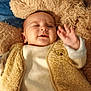 baby, blanket, child, close_up, clothing, cozy, cuddly, cute, fluffy_vest, hand, happy, indoors, infant, portrait, sleepy, smiling, soft_texture, teddy_bear_patch, warm_colors, waving_hand