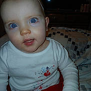 Londyn is registered to the contest to win money with this photo: baby, child, blue_eyes, white_clothing, headband, flower_headband, sitting, indoor, blanket, red_skirt, cute, portrait, face, young_child, infant, person, expression, long_sleeves, furniture, home