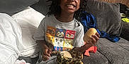 Nyla is registered to the contest to win money with this photo: child, smiling, couch, stuffed_animal, toy, potato, tshirt, flags, wood_paneling, skull, pillow, blanket, carpet, indoor, home, happy, person, seated, living_room, casual