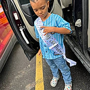Zakari joined the competition — help win amazing prizes! child, birthday, sash, car, open_door, braided_hair, blue_shirt, jeans, colorful_shoes, parking_lot, yellow_line, asphalt, outdoor, casual_clothing, person, standing, daylight, vehicle, door, celebration
