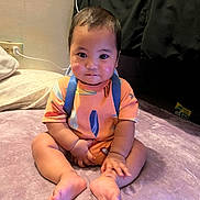 Eziah joined the competition — help win amazing prizes! baby, child, sitting, indoor, blanket, colorful_clothing, orange_outfit, blue_suspender, barefoot, floor, pillow, couch, face, curious_expression, chubby_cheeks, short_hair, person, home, soft_texture, foot