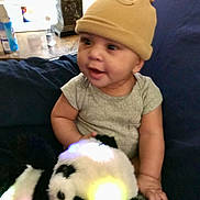 Elijah joined the competition — help win amazing prizes! baby, infant, hat, plush_toy, panda, couch, onesie, smile, sitting, indoor, hand, face, eyes, toy, soft_toy, nightstand, lamp, cozy, blur, cute