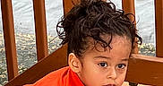 Alexander joined the competition — help win amazing prizes! black_shirt, casual_clothing, child, crawling, curious, curly_hair, daylight, expression, face, hair_tied_up, natural_light, orange_shirt, outdoor, person, playful, skin_tone, wooden_deck, wooden_railings, young_child, young_kid